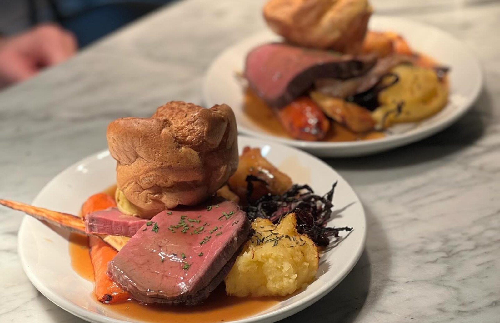 Two plates both with roast beef and all the trimmings including Yorkshire puddings, roasted vegetables and red cabbage.